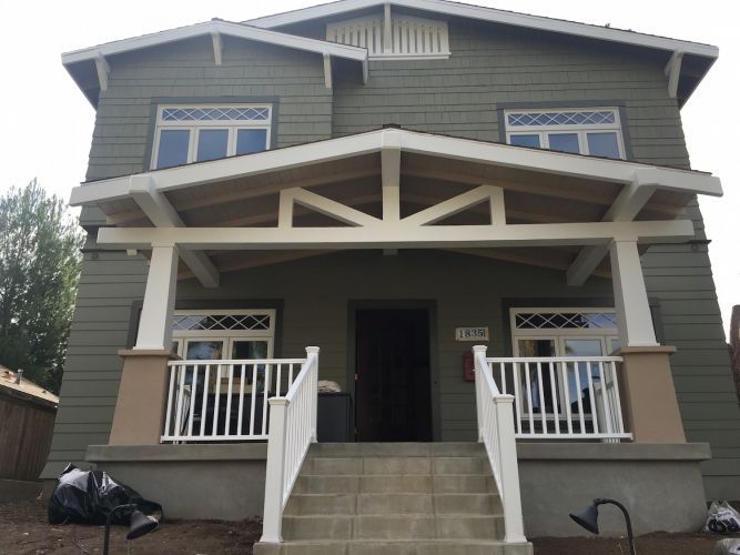 Green two-story house with a porch. White trim, steps, and railings. Brown door and siding.
