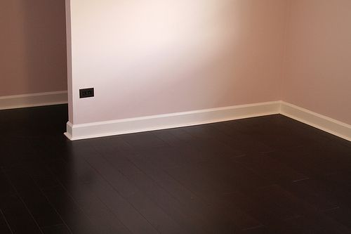 Dark wood floor with light pink walls and white baseboards.