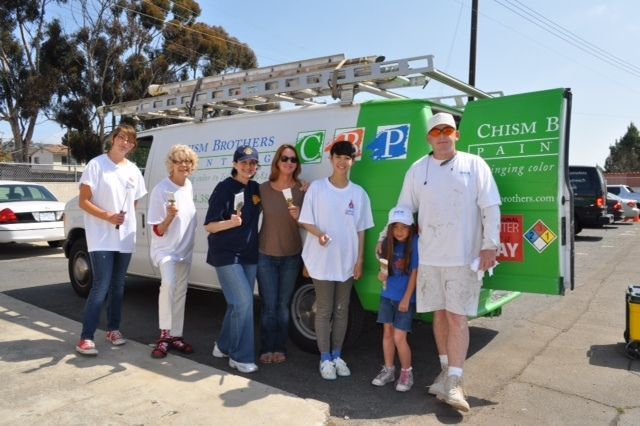 Group of people smiling next to a van; the van has paint company logo and ladder on top.