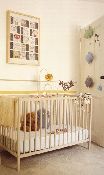 Baby's nursery with light wooden crib, framed artwork, and decorative objects on the door. Yellow and cream tones.