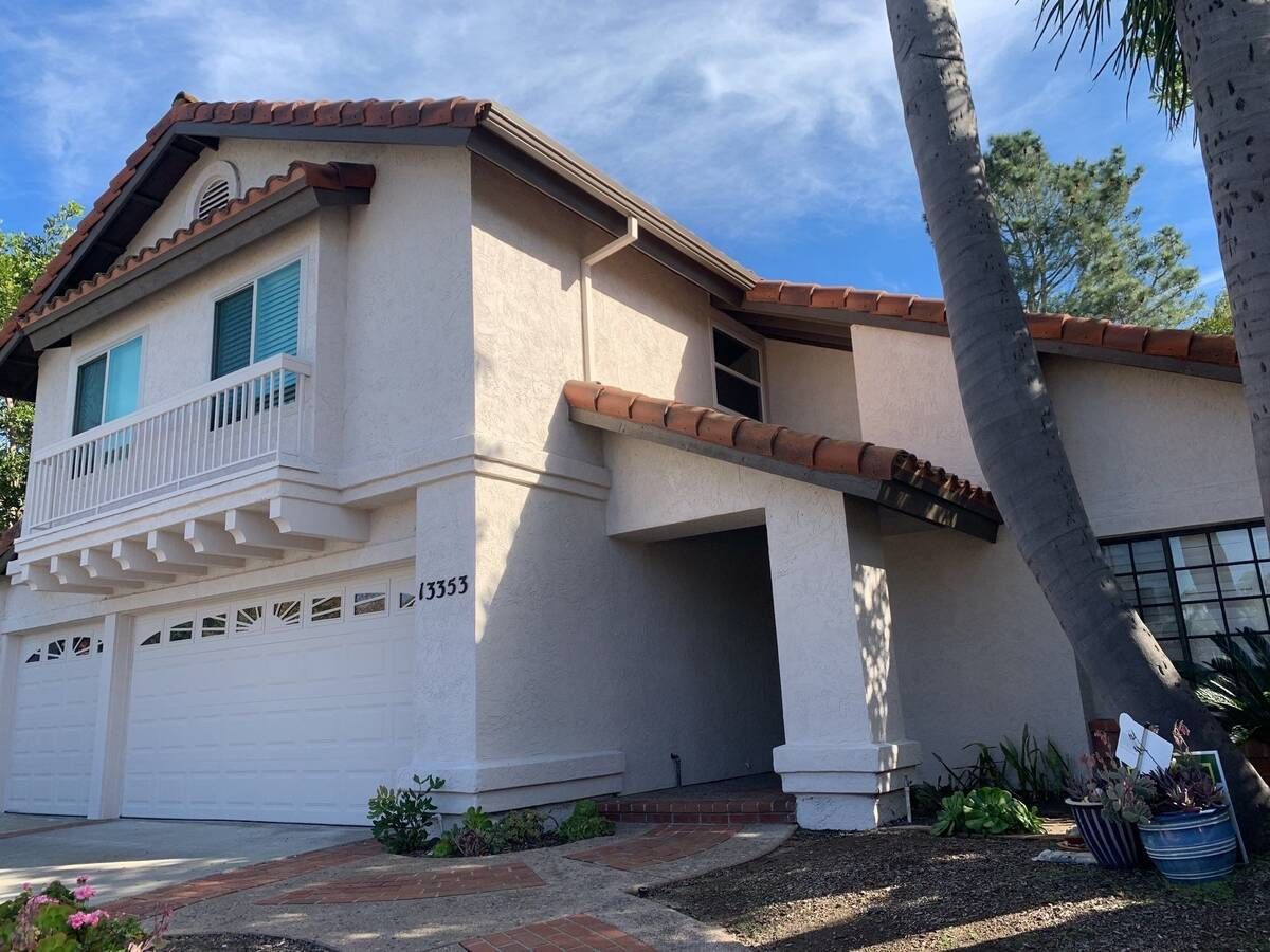 Two-story house with tan stucco, red tile roof, white garage doors, and a balcony.