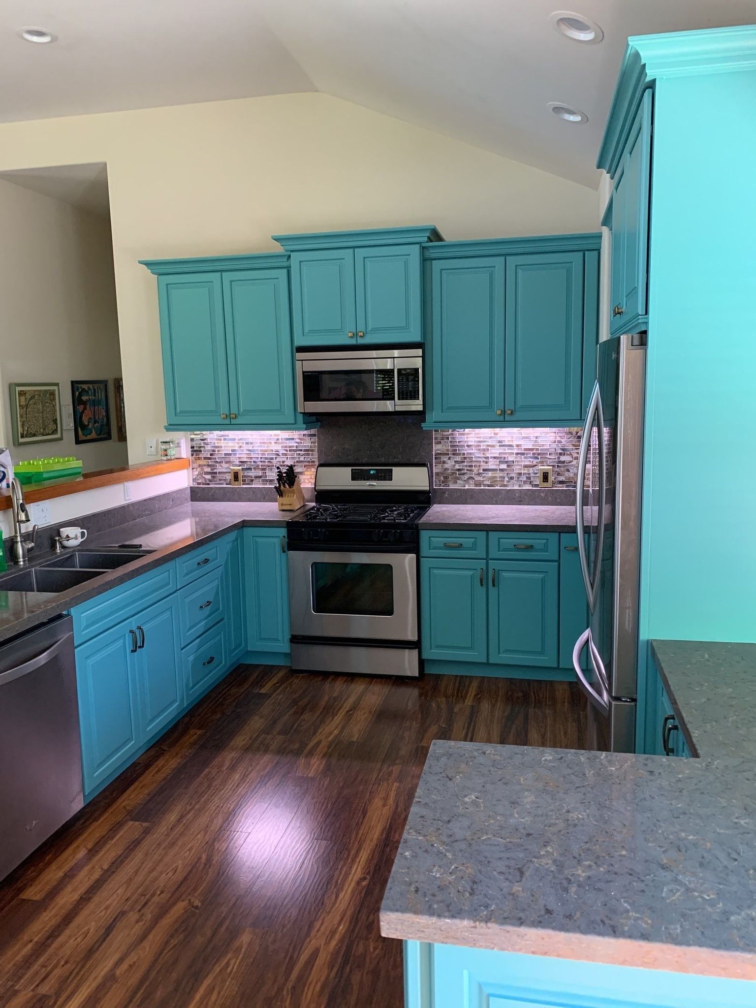 Teal kitchen cabinets, stainless steel appliances, dark countertops, and hardwood floors.