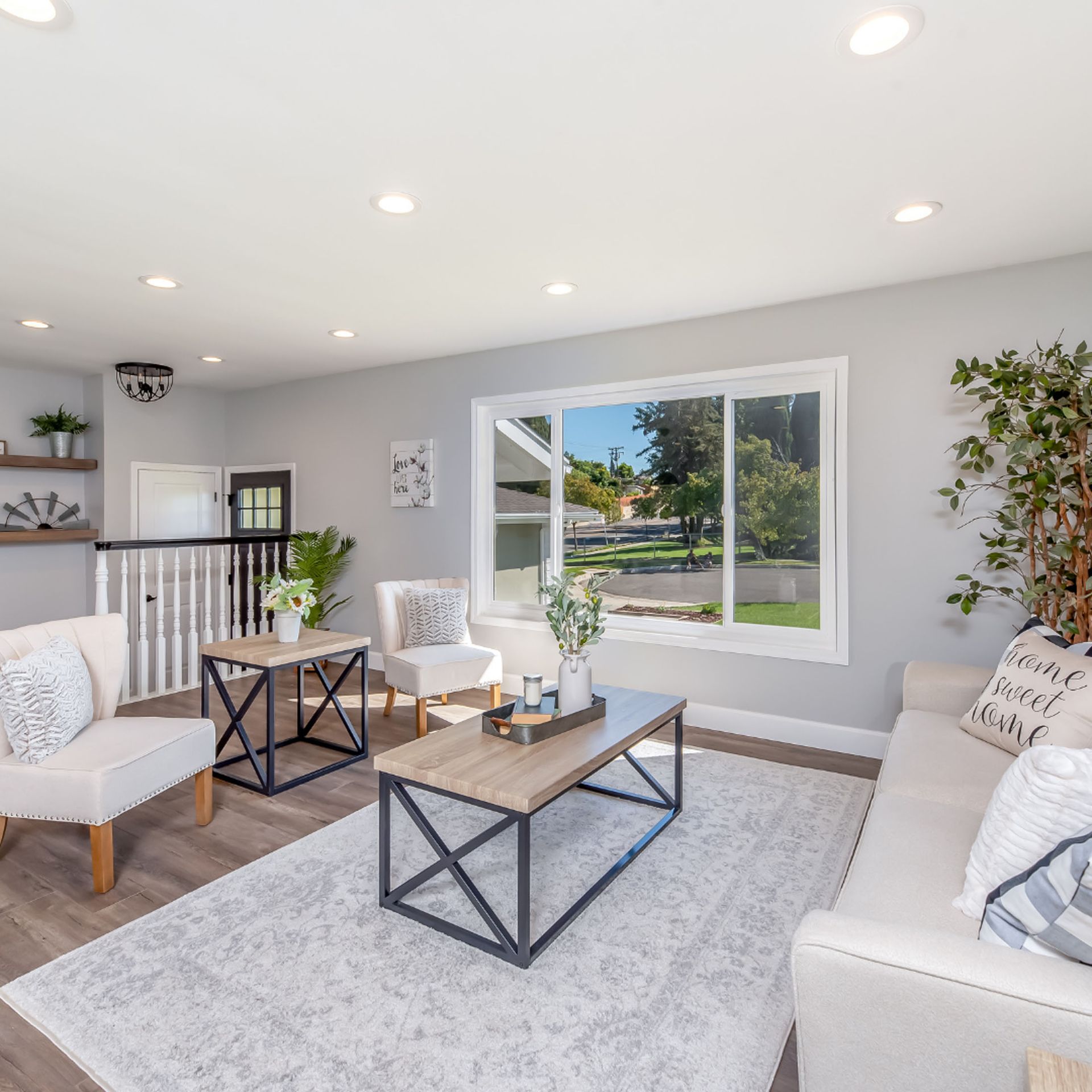Living room with light gray walls, white furniture, and a large window overlooking a yard.