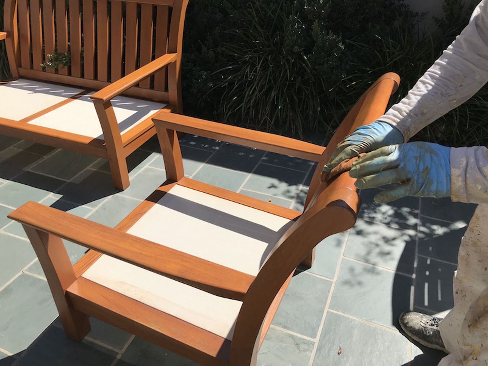 Person in blue gloves staining wooden outdoor furniture.