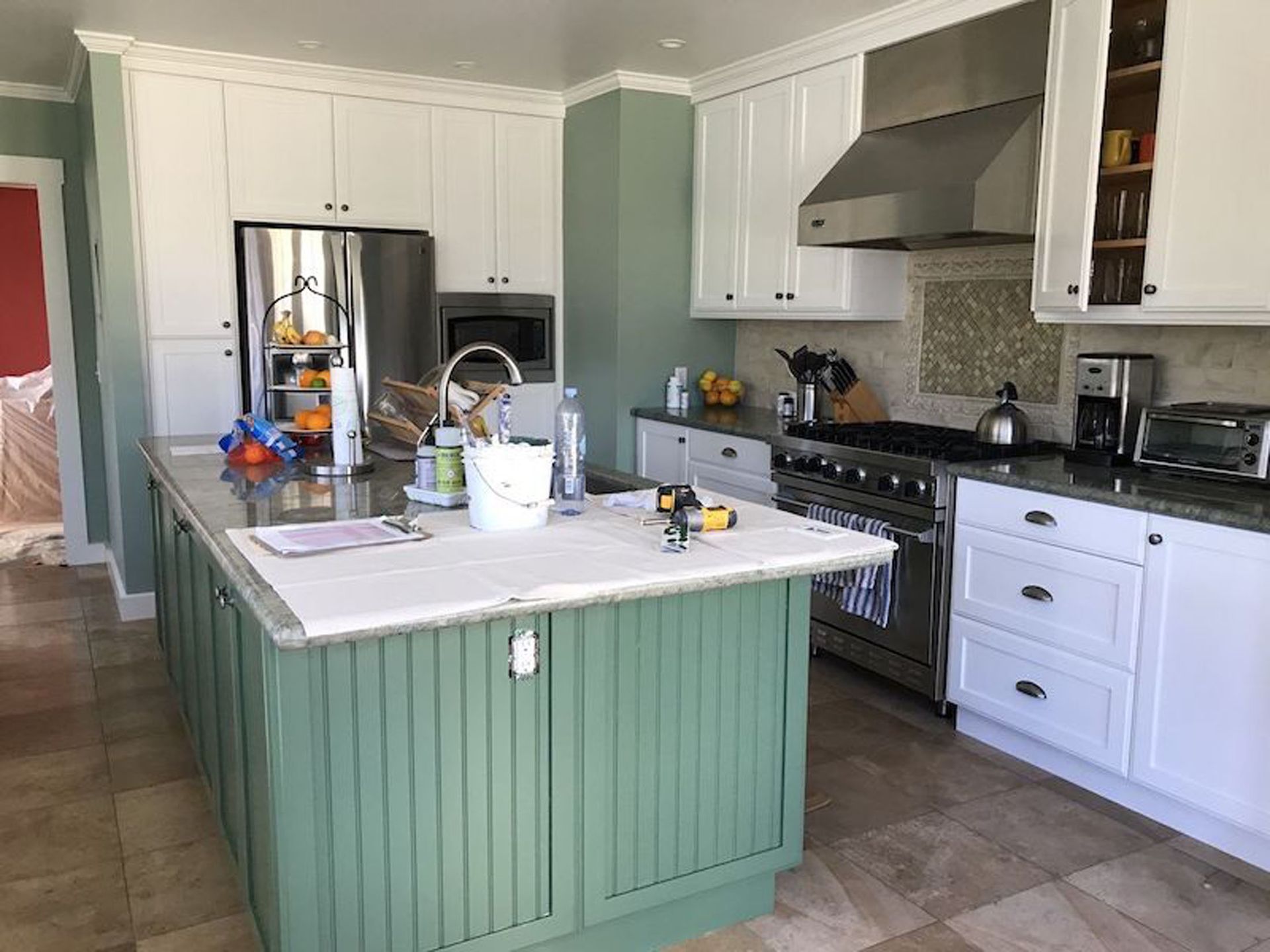 Kitchen with white cabinets, green island, stainless steel appliances, and beige tile floor.