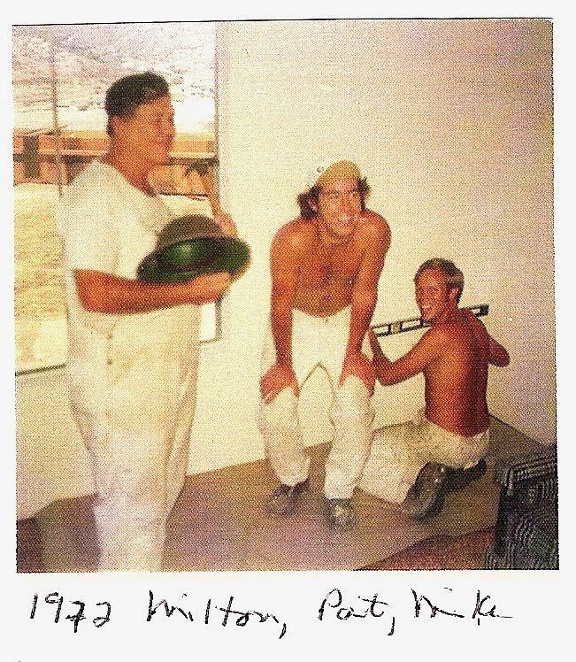Three men in construction clothes pose. One holds a helmet, two others smile with a level. 1972.