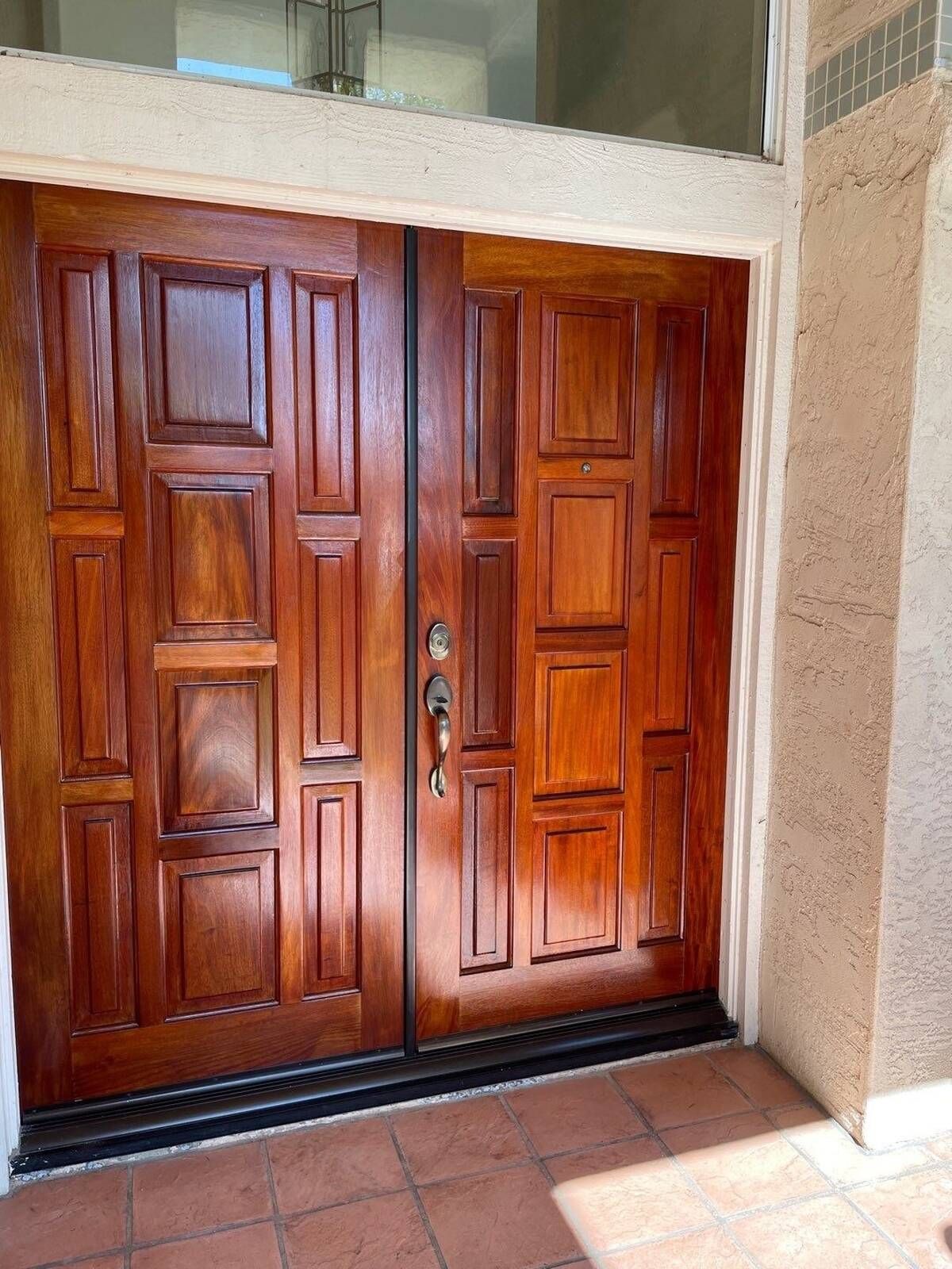 Double wooden doors with a geometric panel design. Brown finish with a dark threshold.