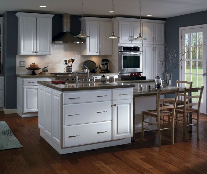 White kitchen with island, cabinets, and oven. Dark countertops, stainless appliances, wooden floor and table.