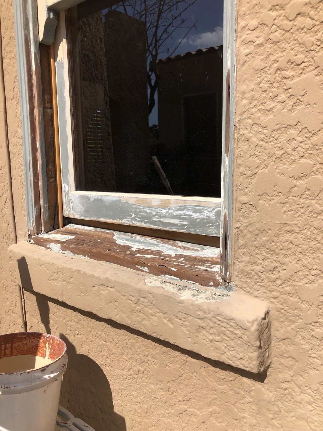 Exterior window with peeling paint and stucco windowsill, reflecting an outside view.