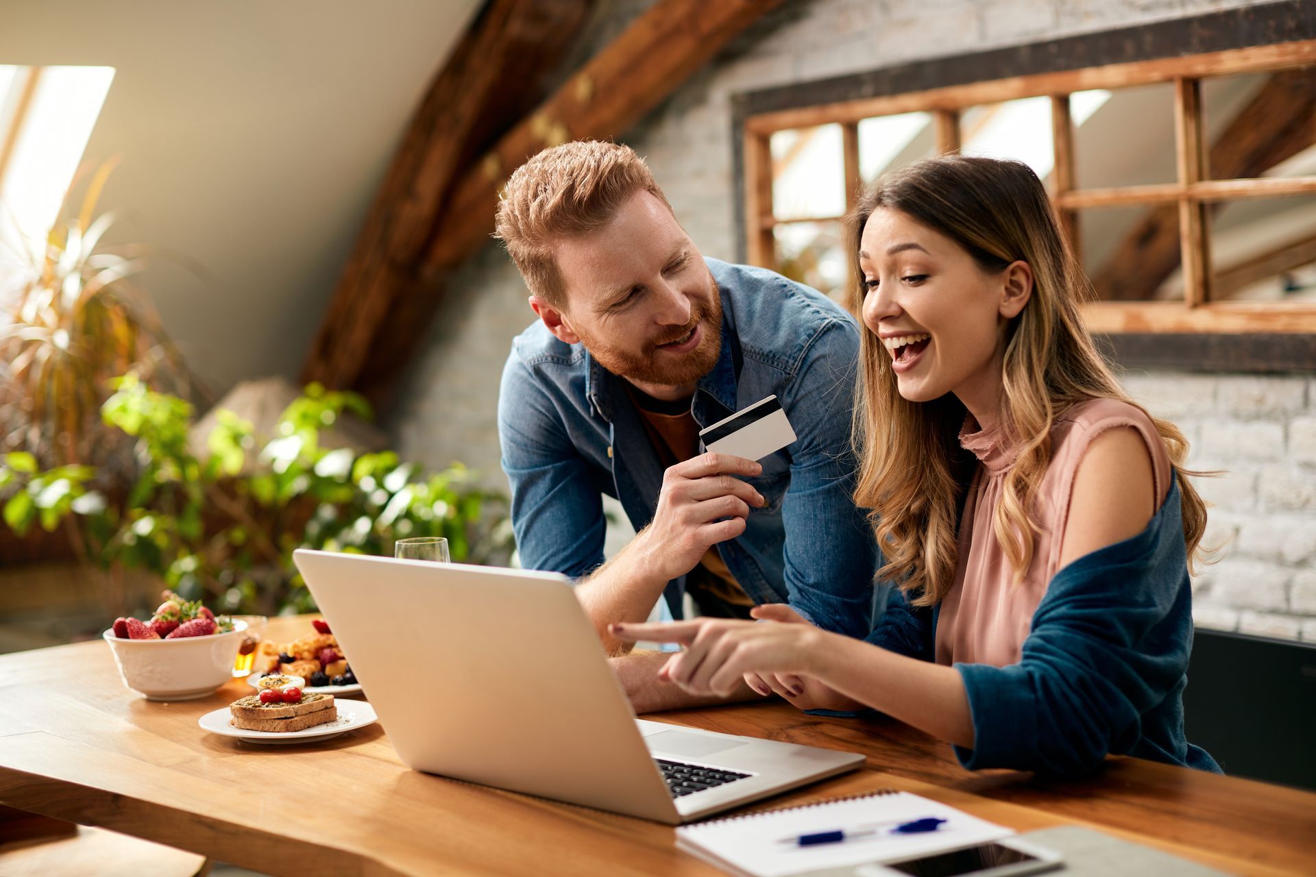 a man holding a credit card and a woman looking at a laptop