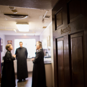 A religious procession with altar servers carrying candles and incense at an altar, in church.