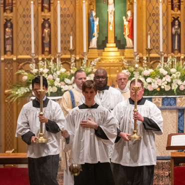 A religious procession with altar servers carrying candles and incense at an altar, in church.
