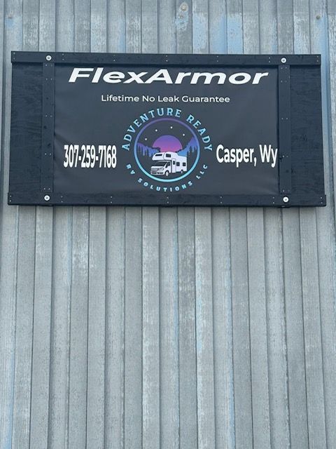 Sign for FlexArmor RV solutions.  Black banner, company logo, phone number, location: Casper, Wy. Mounted on gray corrugated metal.