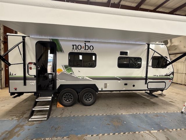 Gray and white NoBo travel trailer with awning extended, two axles, and steps.
