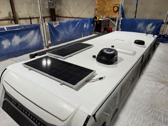 White RV roof with two solar panels, a black dome, and other fixtures.
