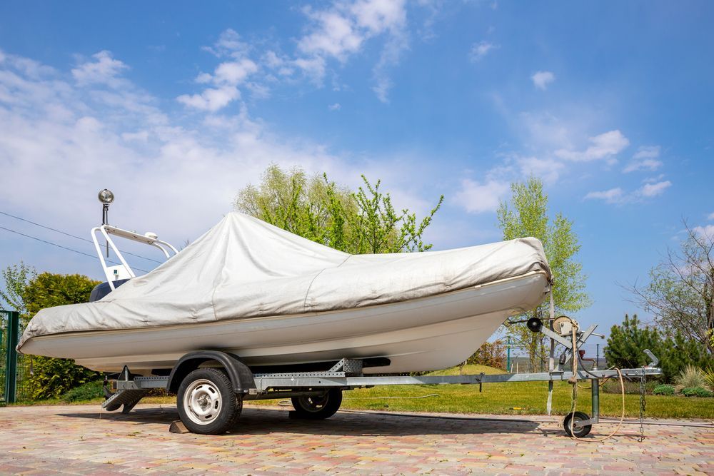 Boat on a trailer, covered with a white tarp, under a blue sky with clouds.