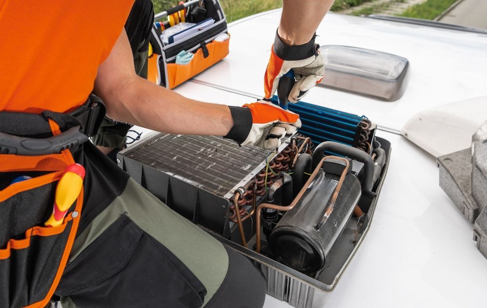 Technician working on an air conditioner unit on a rooftop, wearing gloves and an orange shirt.
