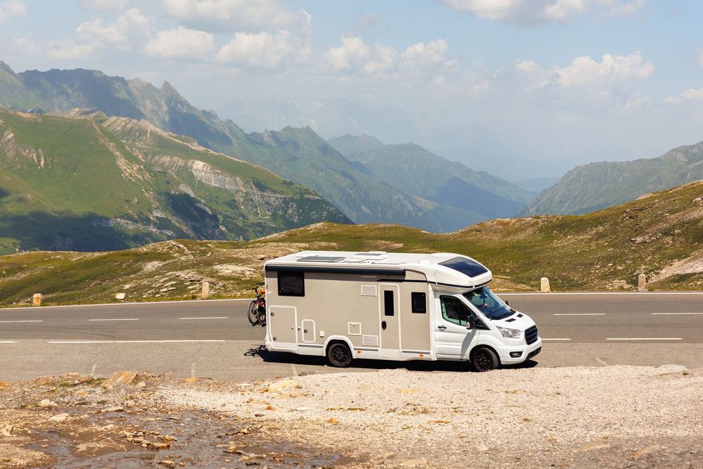 White RV parked on a mountain road with mountain range background.