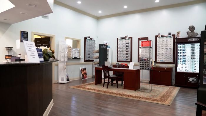 An interior view of an optical shop featuring wooden furniture, wall-mounted glasses displays, and a service desk.