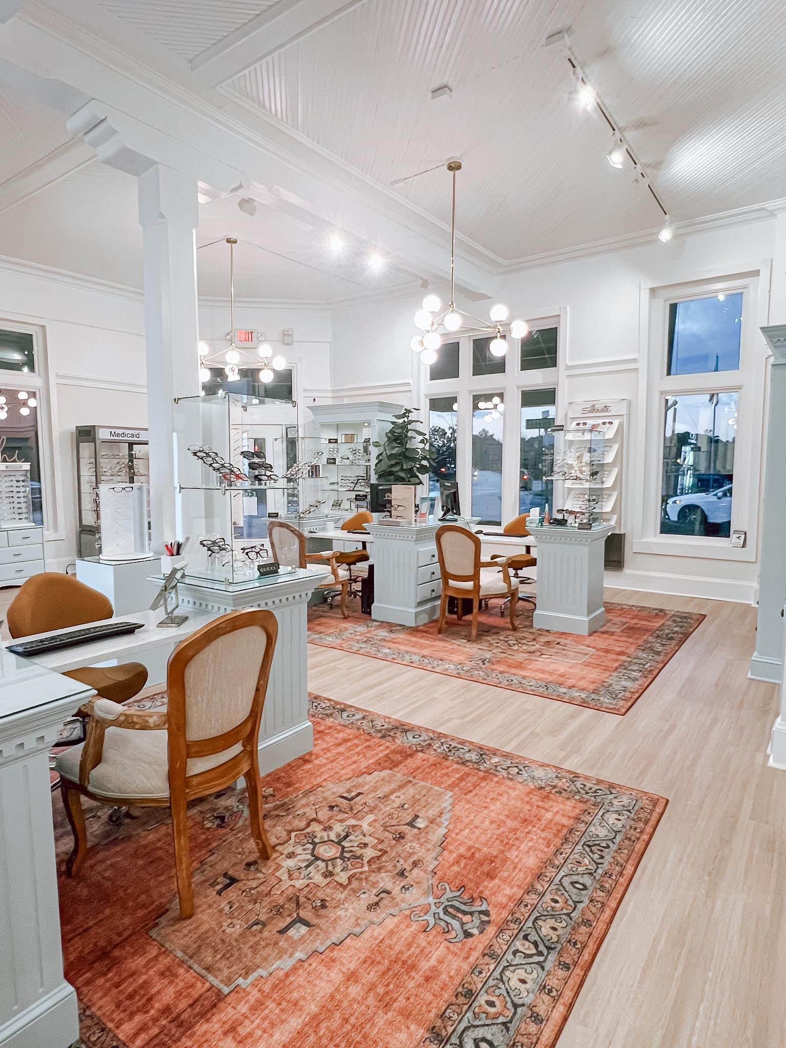 Bright, upscale jewelry store interior featuring white desks, patterned orange area rugs, and ornate chandeliers.