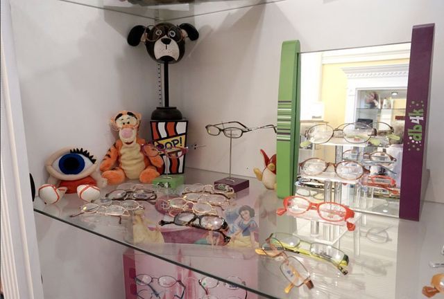 A glass shelf displays several pairs of eyeglasses, a Tigger plush toy, a dog-shaped stand, and a mirror in a store.