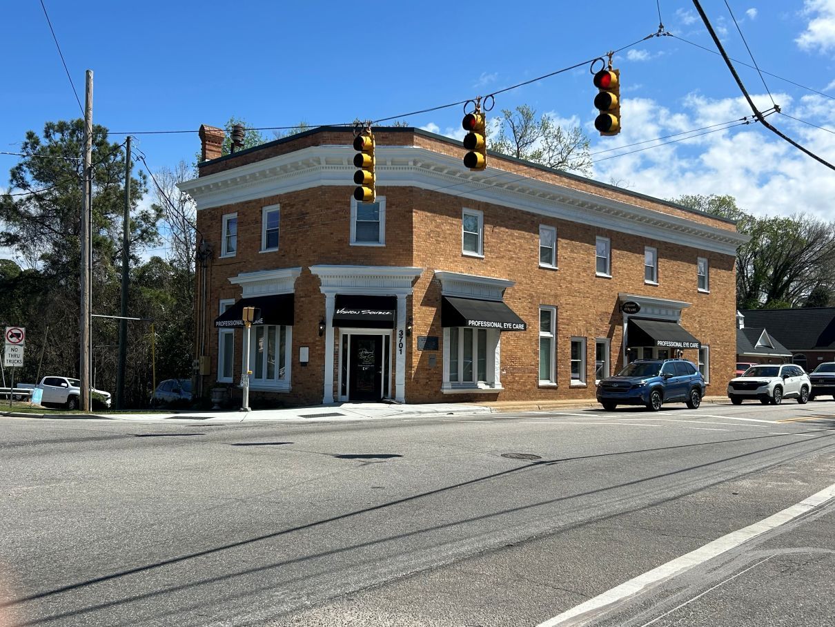 Brick corner building at a street intersection with traffic lights and parked cars on a sunny day in Hope Mills, NC.