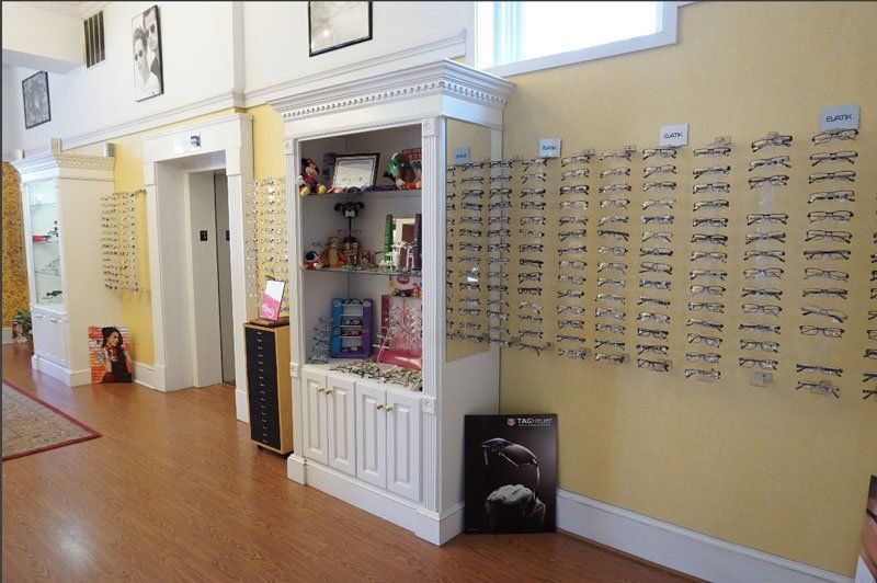 An eye care store interior with rows of eyeglass frames displayed on a yellow wall next to a white display cabinet.