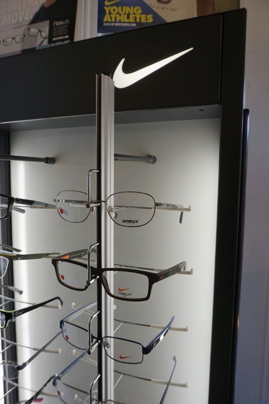A black Nike branded display stand featuring multiple pairs of eyeglasses on white illuminated shelves.