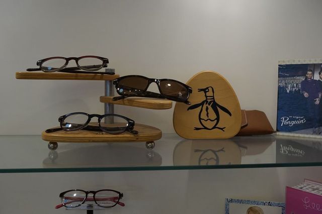 Eyeglasses displayed on a multi-tiered wooden stand next to a penguin-shaped sign on a glass shelf.