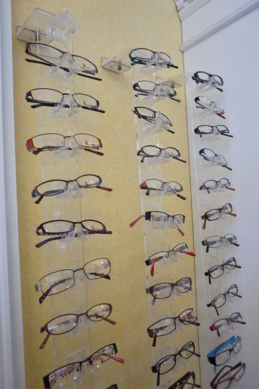 A wall-mounted display rack in an optical store featuring three vertical columns of assorted eyeglasses.