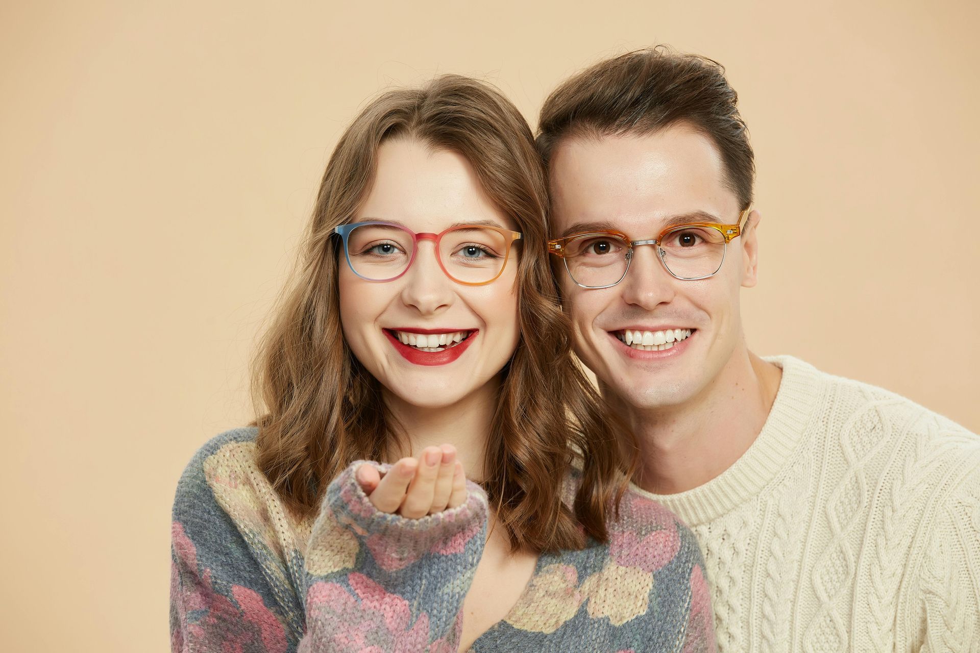 A smiling couple wearing light-colored, patterned glasses against a plain beige background.