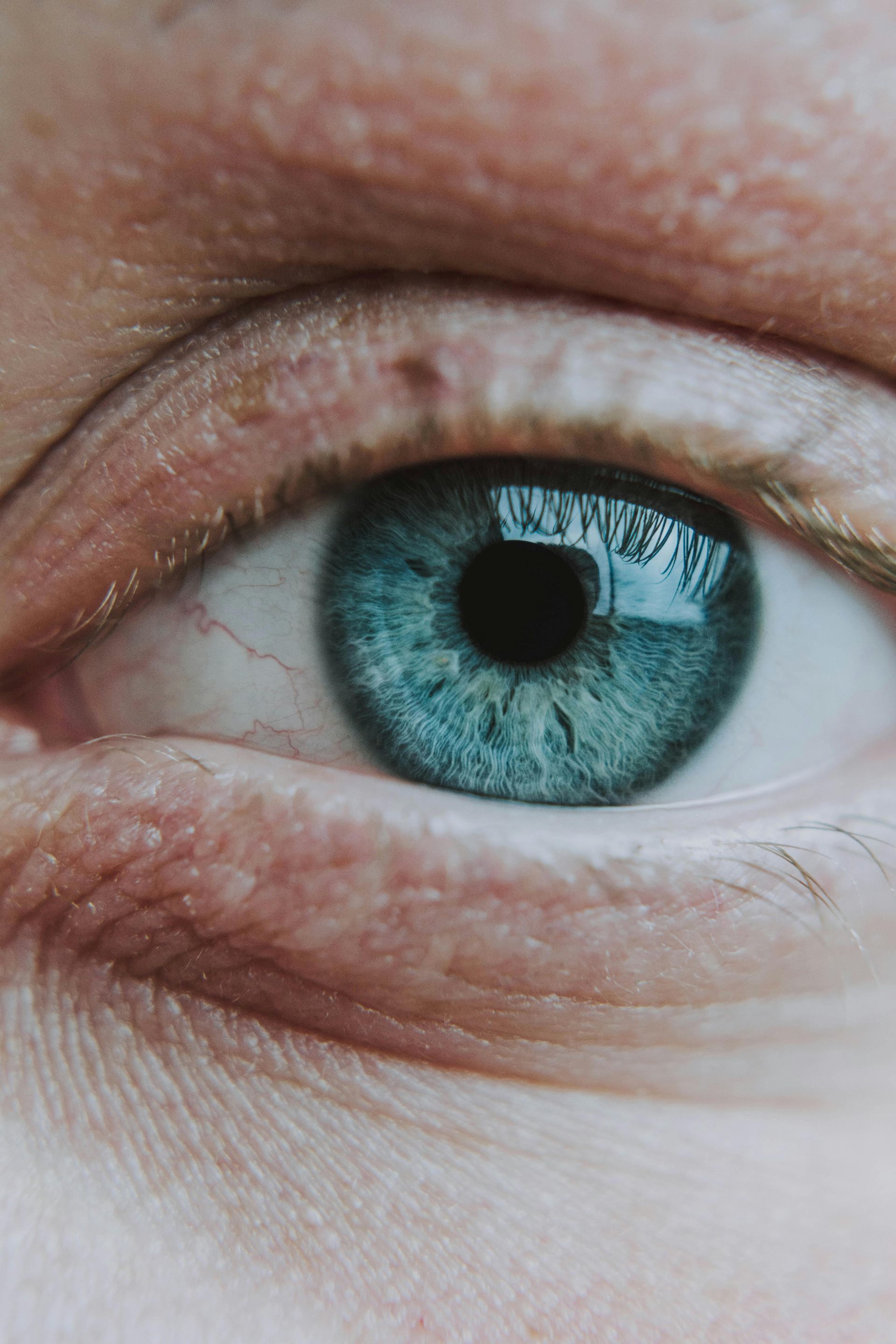 A close-up of a human eye with a bright blue iris and detailed texture, viewed in soft light.