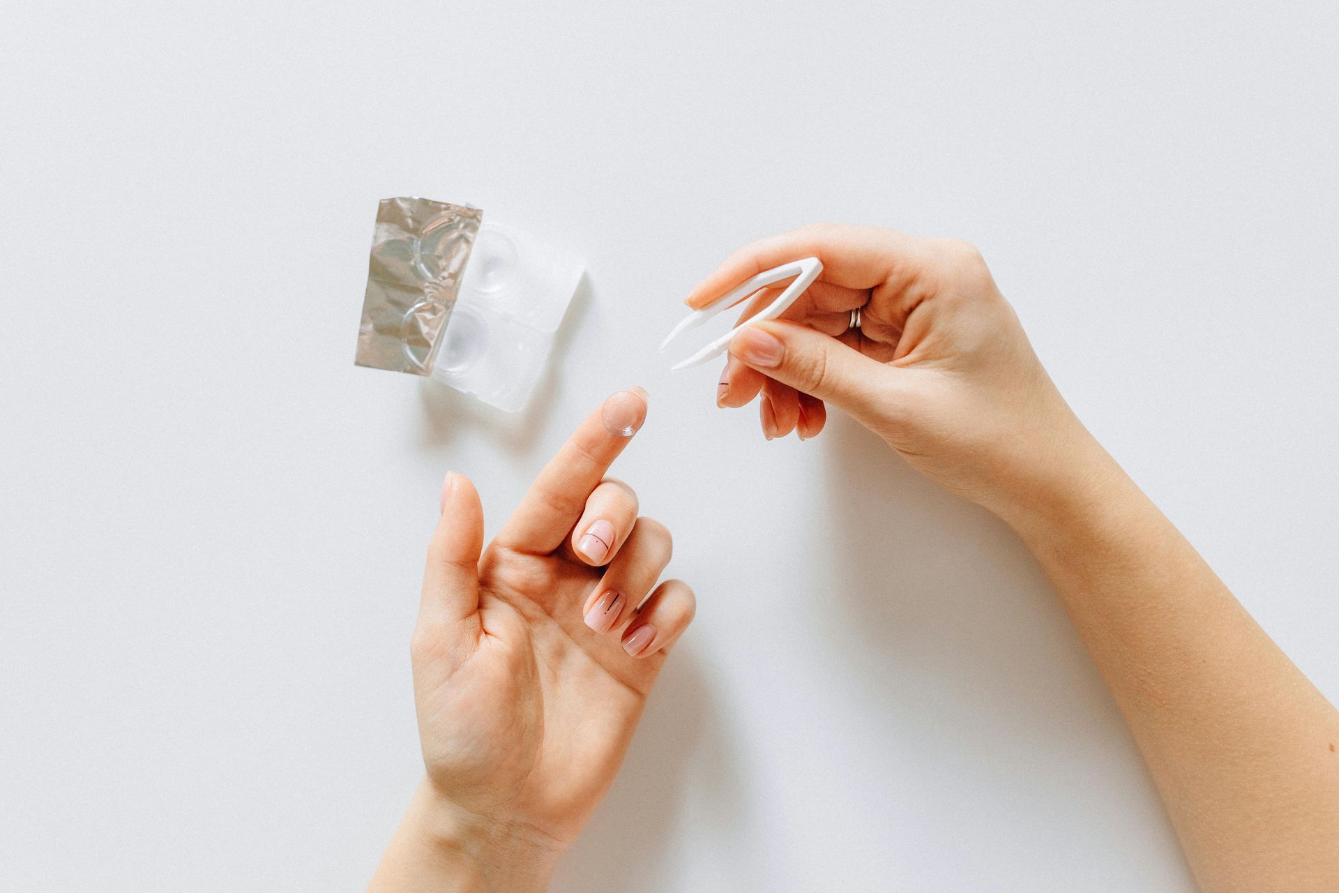Hands using tweezers to place a small, white medical device onto a fingertip near a foil wrapper.