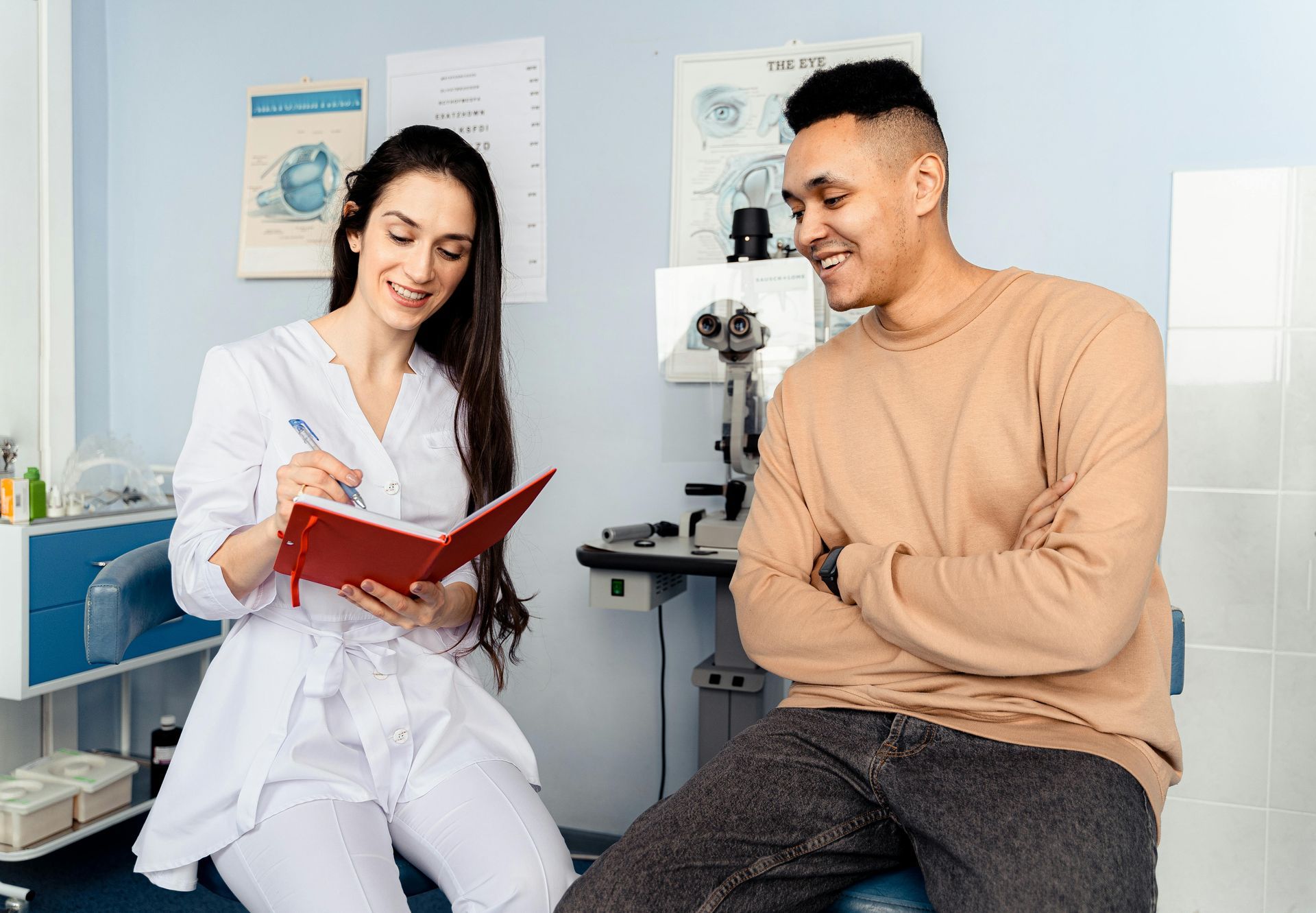 A professional in a white coat writes in a notebook while a patient listens in an eye clinic.