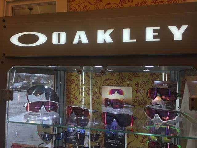 An Oakley-branded display case featuring several pairs of performance sunglasses on shelves against a floral background.