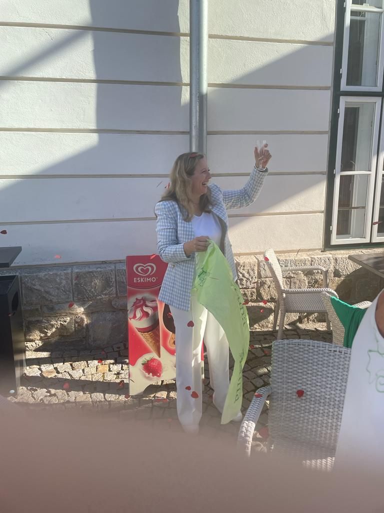 A woman is standing in front of a building holding a glass of wine.