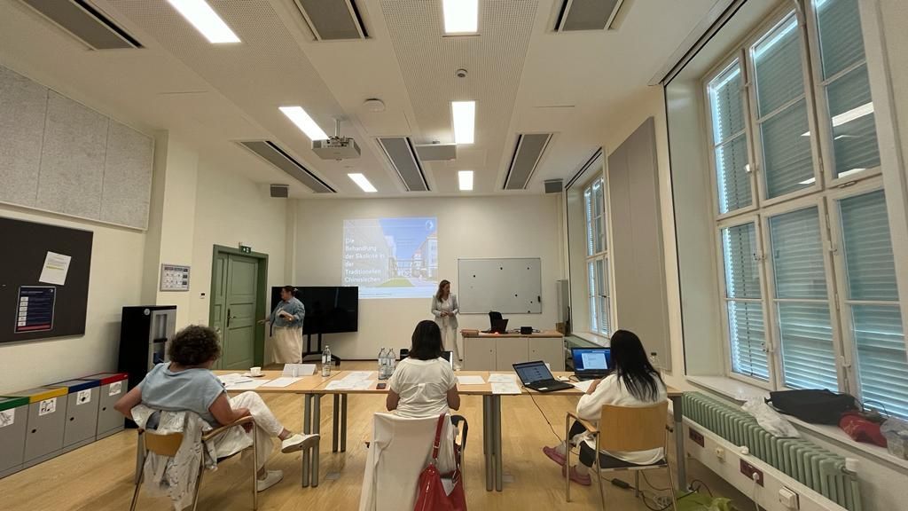 A group of people are sitting at tables in a room with a projector screen.