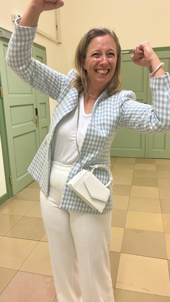 A woman in a blue jacket and white pants is flexing her muscles.