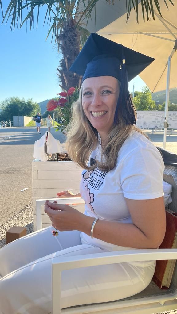 A woman wearing a graduation cap and gown is sitting in a chair.