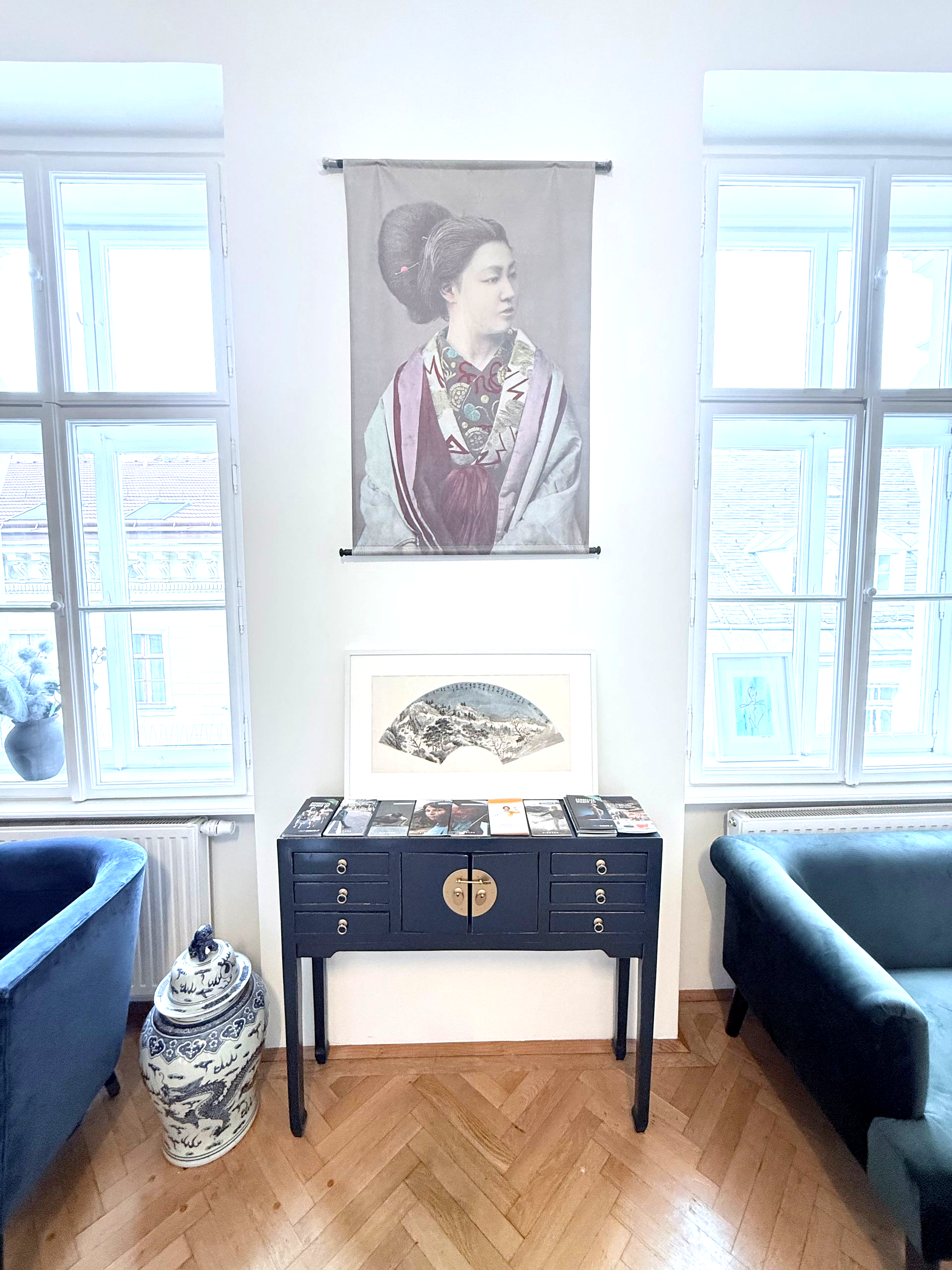 Eine Frau sitzt mit einem Laptop an einem Schreibtisch in einem Zimmer.