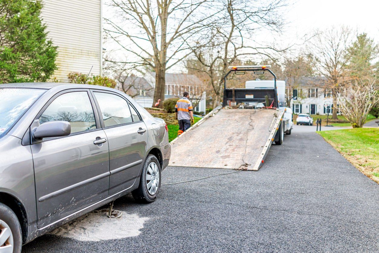 A tow truck is towing a car in a driveway.