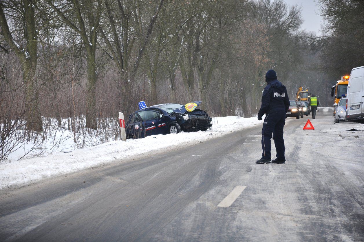 A police officer dressed in black clothing directing traffic while overseeing a winch out from a vehicle stuck in a snow covered ditch.