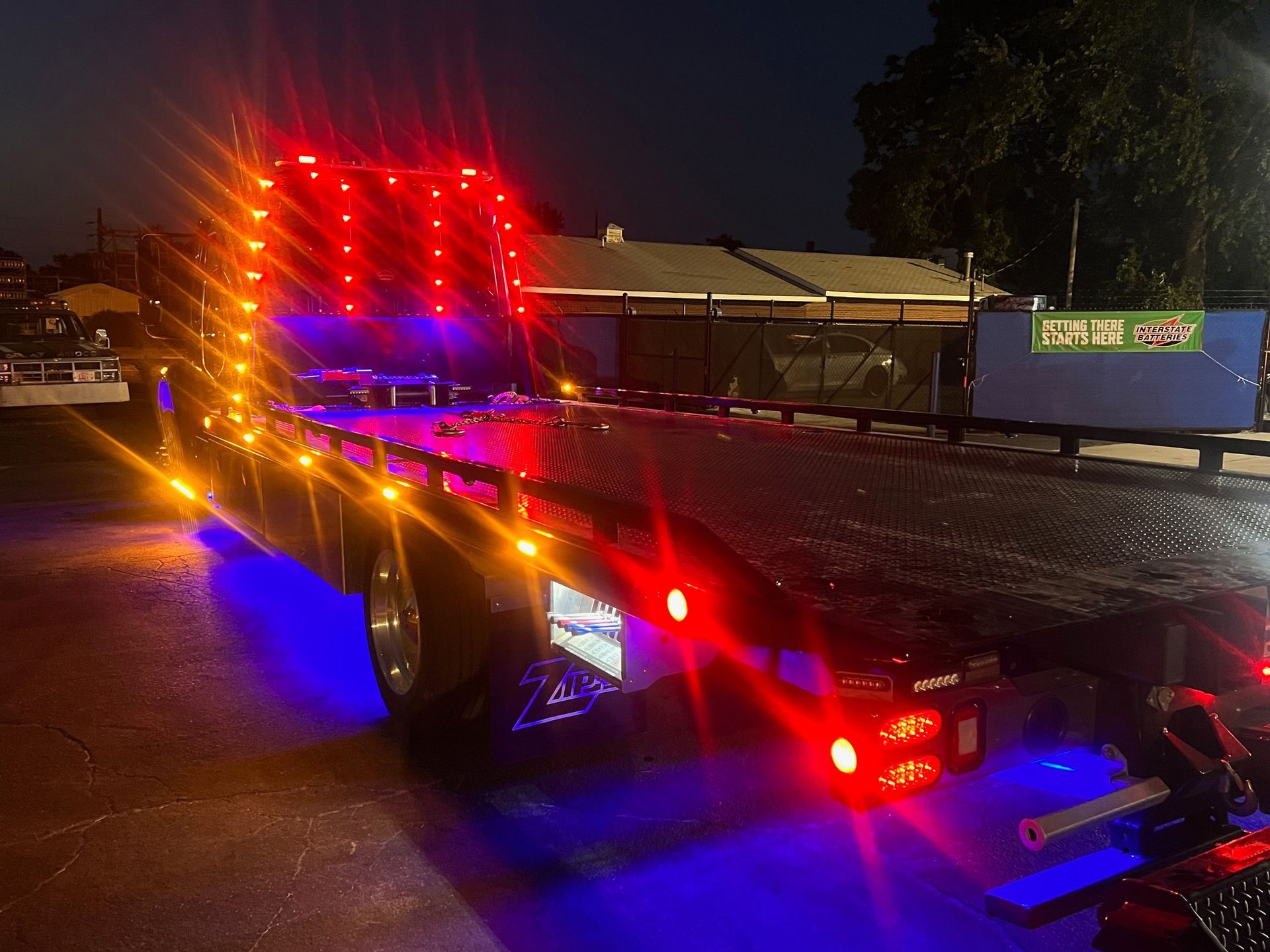 A blue tow truck in the dark being illuminated by its orange and red lights