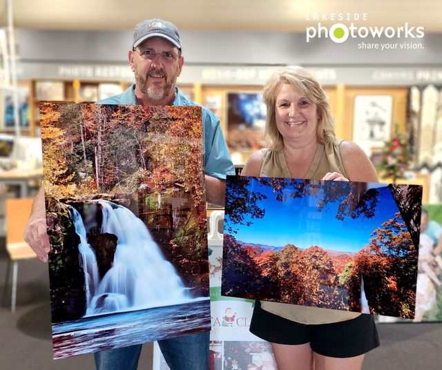 Two people holding large autumn landscape prints inside a photo shop