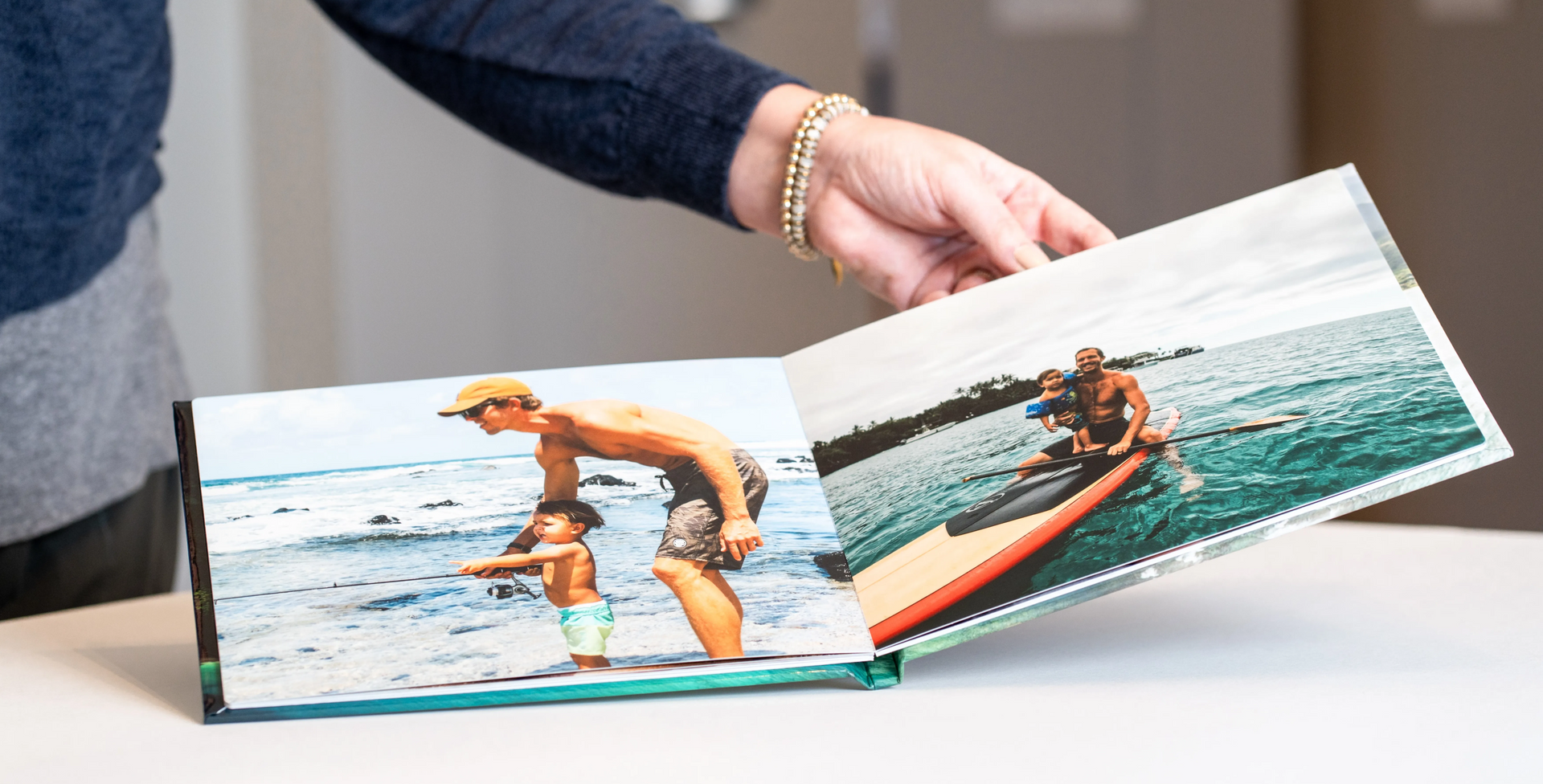 Hand flipping through a photo book showing surf action shots on a white table