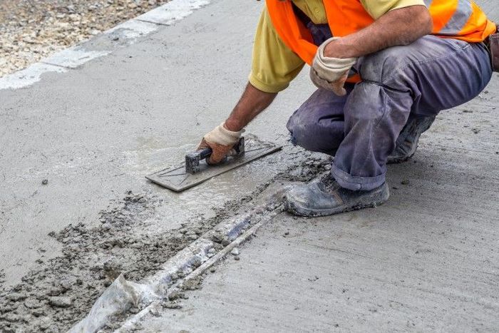 Construction worker smoothing concrete with a trowel, wearing a safety vest and gloves.