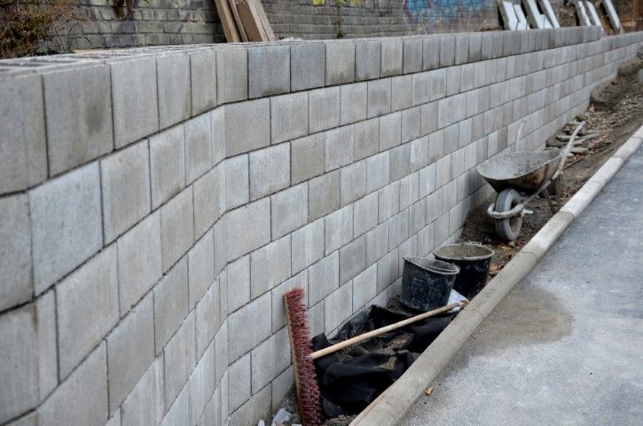 Gray block retaining wall along a roadway, with construction materials visible.