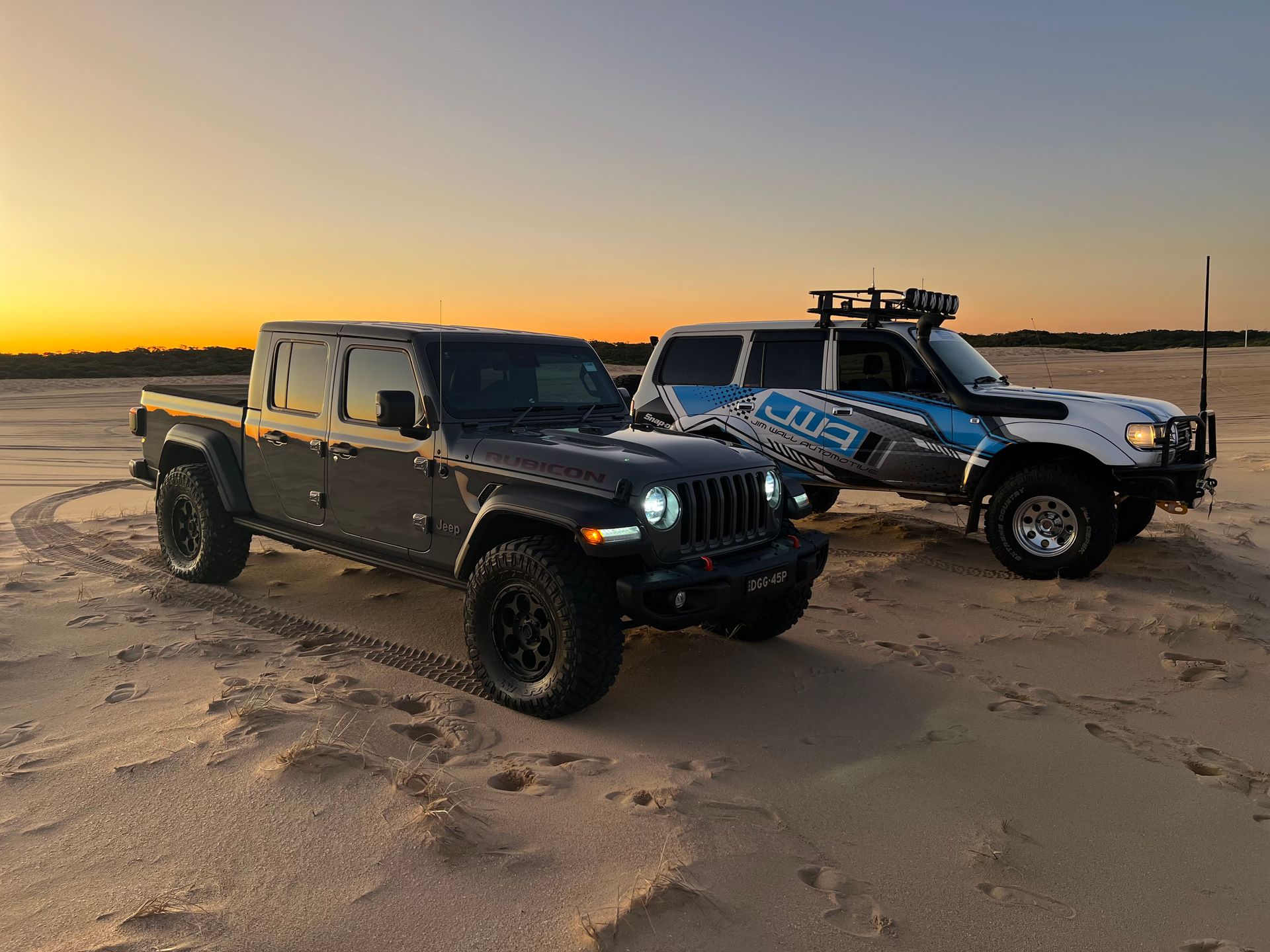 Two work vehicles parked on sand at sunset β Jim Wall Automotive in Mittagong, NSW