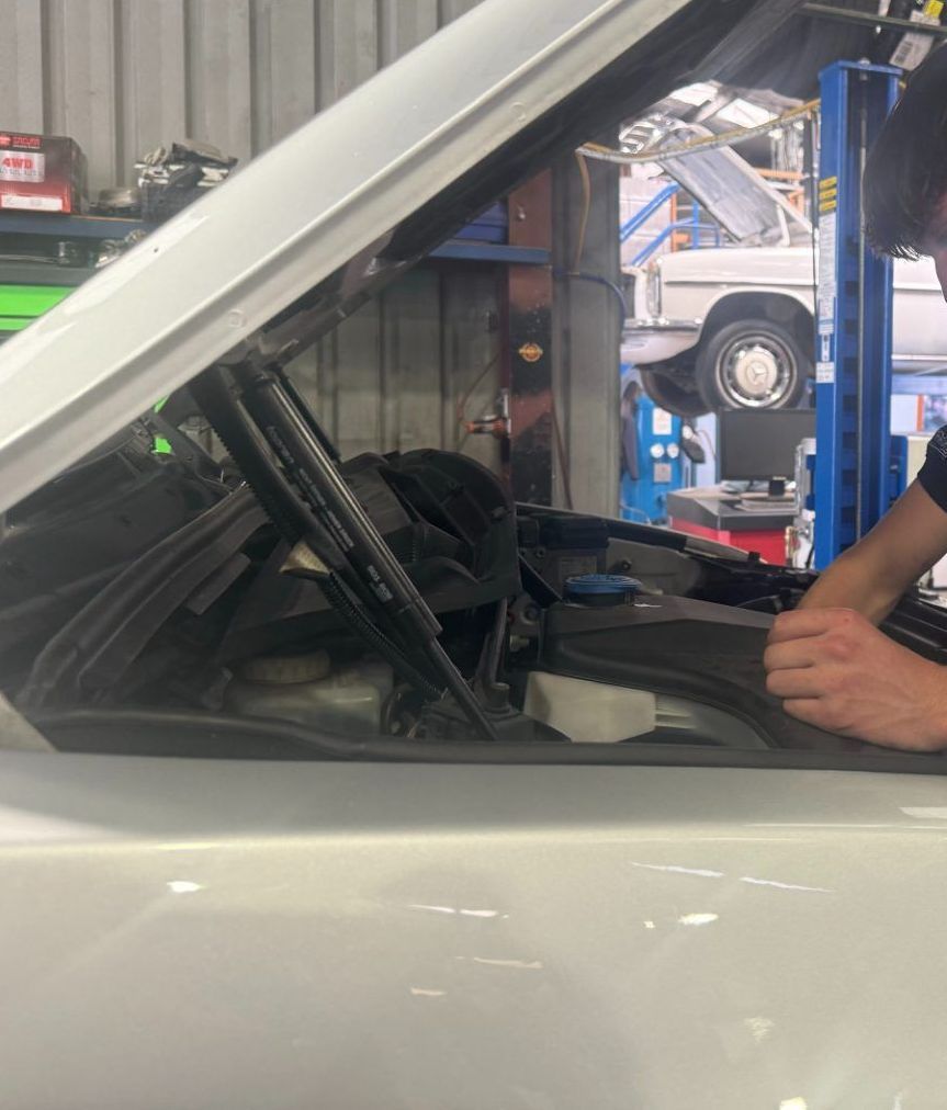 A hood of a car is open and someone is reaching in — Jim Wall Automotive in Mittagong, NSW