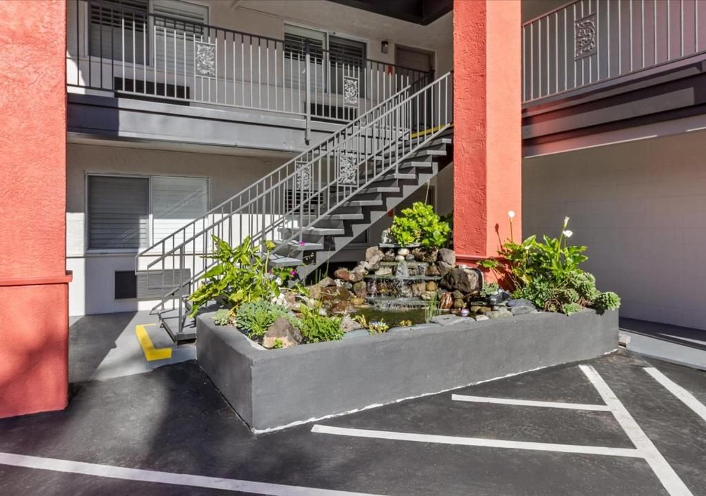 An outdoor staircase with metal railings leads to a second-floor walkway, situated above a concrete garden bed.